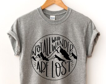 以下が含まれることがあります： 山脈と「Not all who wander are lost」というテキストが描かれた黒い円形のグラフィックが施されたグレーのTシャツです。