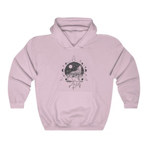 Pode incluir: Uma camisa de moletom rosa com capuz com uma estampa gr&aacute;fica em preto e branco de um lobo uivando para a lua. O gr&aacute;fico tamb&eacute;m inclui um ciclo de fases lunares, um tri&acirc;ngulo e um apanhador de sonhos.