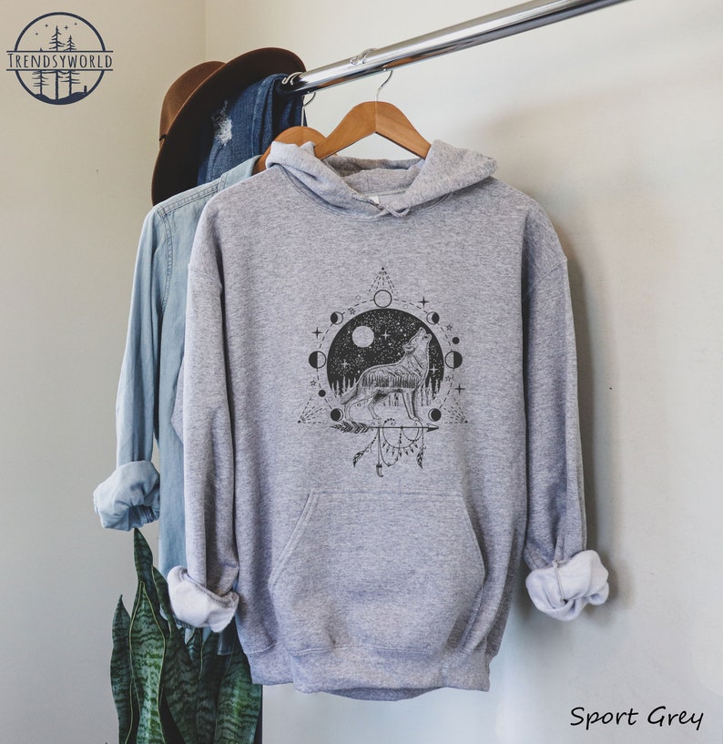 Pode incluir: Uma camisa de moletom cinza com capuz com uma estampa gr&aacute;fica em preto e branco de um lobo uivando para a lua. O gr&aacute;fico tamb&eacute;m inclui um ciclo de fases lunares, estrelas e um design geom&eacute;trico. O texto "Sport Grey" &eacute; vis&iacute;vel na parte inferior da imagem.