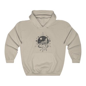Pode incluir: Uma camisa de moletom com capuz bege com uma estampa gr&aacute;fica em preto e branco de um lobo uivando para a lua. O gr&aacute;fico tamb&eacute;m inclui um c&iacute;rculo de luas, estrelas e um tri&acirc;ngulo.