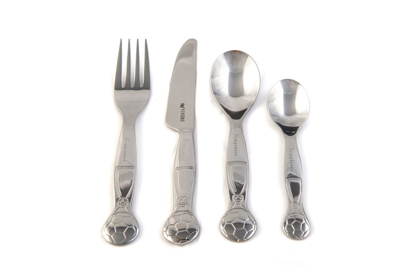 May include: A set of four stainless steel children's cutlery with a soccer ball design. The set includes a fork, knife, and two spoons.