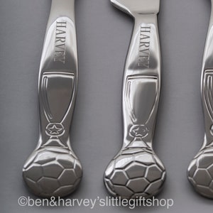 May include: Three silver-colored, personalized children's cutlery sets with a soccer ball design. Each handle is engraved with the name "Harvey".