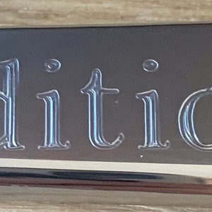 May include: A silver metal plaque with the word "Traditional" engraved in a script font.