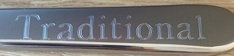 May include: A silver metal plaque with the word "Traditional" engraved in a script font.