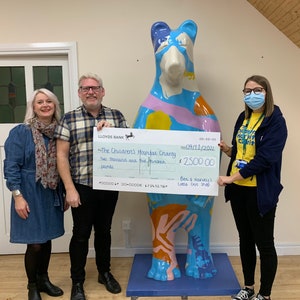 May include: A check for two thousand five hundred pounds is being presented to The Children's Hospital Charity by Ben & Harvey's Little Gift Shop. The check is dated 09/11/2021. The check is being presented in front of a colorful bear sculpture.