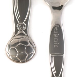 May include: A set of three silver spoons with a soccer ball design. The spoon on the right has the name "Benjamin" engraved on it.