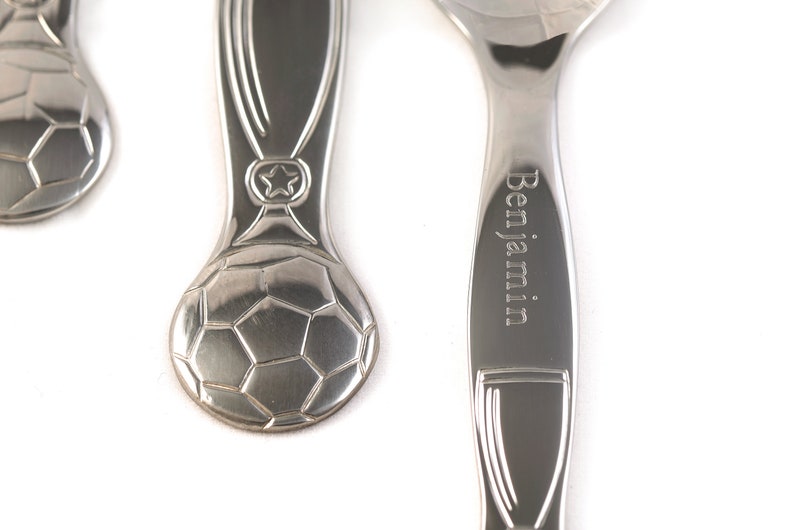 May include: A set of three silver spoons with a soccer ball design. The spoon on the right has the name "Benjamin" engraved on it.