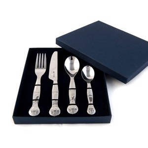 May include: A set of four stainless steel children's cutlery pieces in a blue box. The set includes a fork, knife, and two spoons. The handles of the cutlery are decorated with a textured design.