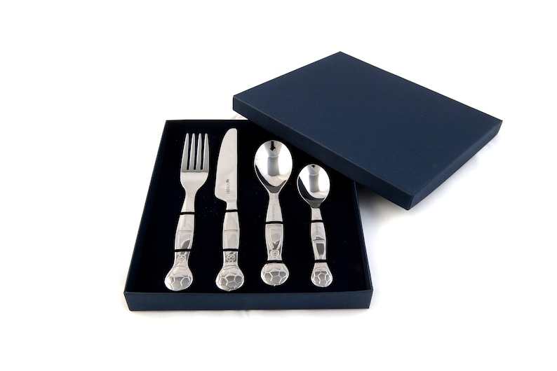 May include: A set of four stainless steel children's cutlery pieces in a blue box. The set includes a fork, knife, and two spoons. The handles of the cutlery are decorated with a textured design.