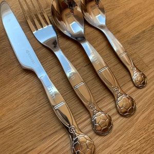May include: Set of four silver-toned utensils with a soccer ball design on the handles. The utensils include a knife, fork, and two spoons. The words "Kim" and "Winners" are engraved on the handles.