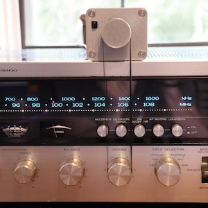 K&ouml;nnte beinhalten: Vintage silberner Receiver, Modell KR-9400, mit beleuchteter Frequenzanzeige und Abstimmrad. Verschiedene Bedienkn&ouml;pfe sind sichtbar. Ein silbernes Ger&auml;t ist oben montiert und mit einem schwarzen Draht verbunden. Das Display zeigt Frequenzen in kHz und MHz an.