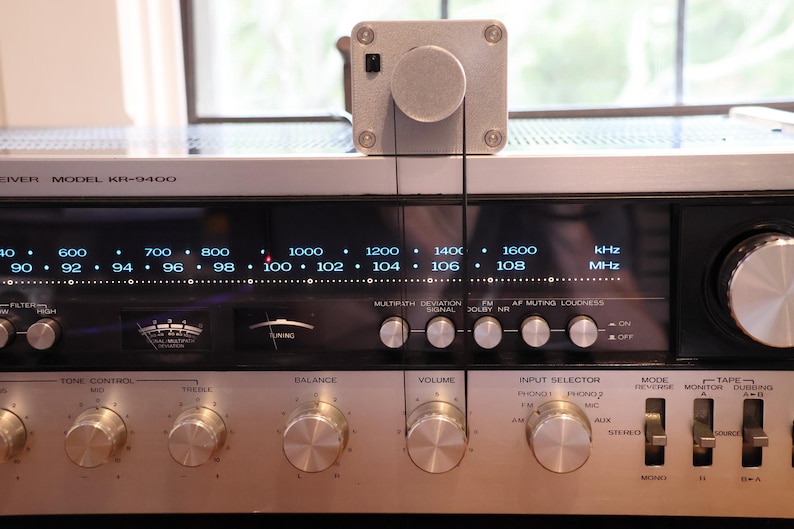 K&ouml;nnte beinhalten: Vintage silberner Receiver, Modell KR-9400, mit beleuchteter Frequenzanzeige und Abstimmrad. Verschiedene Bedienkn&ouml;pfe sind sichtbar. Ein silbernes Ger&auml;t ist oben montiert und mit einem schwarzen Draht verbunden. Das Display zeigt Frequenzen in kHz und MHz an.