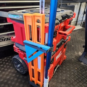 May include: A red toolbox with a blue and orange tool holder attached to the side. The tool holder has a blue triangle and two orange rulers.