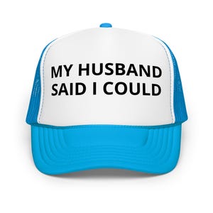 May include: A trucker hat with a white front panel and a bright blue brim and mesh back. The text "MY HUSBAND SAID I COULD" is printed in black on the front panel. The hat has a curved brim and a snapback closure.