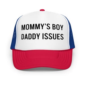 Może przedstawiać: Czapka typu trucker w kolorze czerwonym, białym i niebieskim z napisem "MOMMY'S BOY DADDY ISSUES" pogrubionymi czarnymi literami. Czapka ma biały panel przedni, czerwony daszek i niebieski tył z siatki.