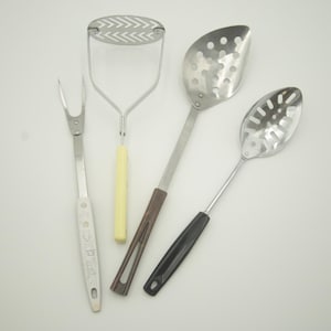 May include: Four kitchen utensils: a silver potato masher with a yellow handle, a silver slotted spoon with a brown handle, a silver slotted spoon with a black handle, and a silver fork with a silver handle.