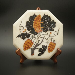 Puede incluir: Posavasos octogonal de mármol blanco con un diseño de vides y hojas incrustadas en negro y marrón.