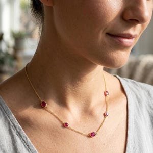 May include: A gold necklace with oval ruby gemstones. The necklace has a fine gold chain with evenly spaced, vibrant red gemstones. The gemstones are a deep red colour, contrasting with the gold chain. The necklace is a simple yet elegant piece of jewellery.
