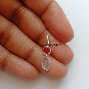 May include: A silver pendant featuring a teardrop-shaped clear stone and a round red stone.