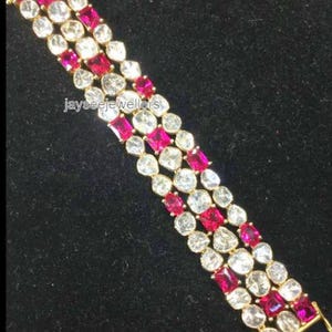 May include: A gold bracelet with a multi-row design featuring alternating pink and white gemstones. The bracelet is made with a delicate gold chain and features a variety of round and rectangular gemstones.