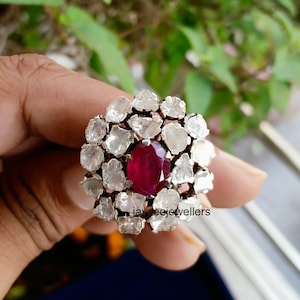 May include: A silver ring with a large red gemstone surrounded by smaller white gemstones. The ring is set in a floral design. The text "jayceejewellers" is visible on the ring.