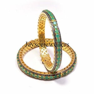 Op de afbeelding: Twee gouden armbanden met een rij groene edelstenen en een rij kleinere zilveren edelstenen rond de omtrek.