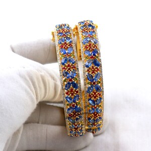May include: A pair of gold bangles with blue, red, and white gemstones set in a floral pattern.