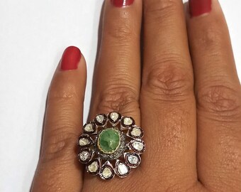 May include: A silver ring featuring a green gemstone surrounded by smaller diamonds. The ring is set in a floral design with a red accent.