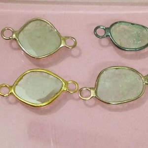 Op de afbeelding: Vier edelsteen-connector charms met gouden en zilveren instellingen. De charms zijn traanvormig en hebben een heldere, gefacetteerde edelsteen.