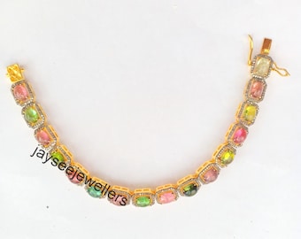 May include: A gold bracelet with a row of colorful oval gemstones set in square frames. The gemstones are pink, green, and yellow. The bracelet has a clasp closure.