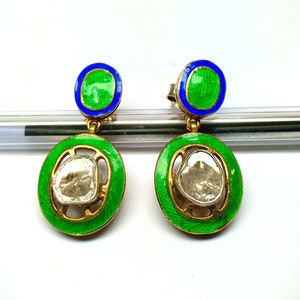 May include: A pair of gold earrings with green and blue enamel. Each earring features a round, clear diamond-like stone set in a gold frame.