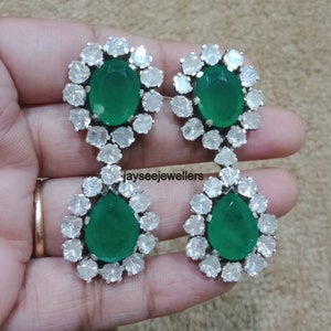 May include: A pair of dangle earrings with green oval and pear-shaped gemstones surrounded by a halo of white stones.
