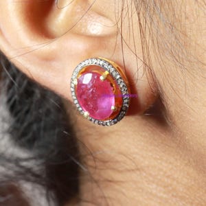 May include: A pair of gold earrings with a pink gemstone surrounded by a halo of small diamonds.