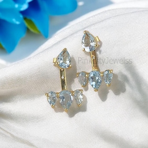 Pode incluir: Um par de brincos de ouro com uma gema azul em forma de lágrima na parte superior e três gemas azuis menores em forma de lágrima na parte inferior.