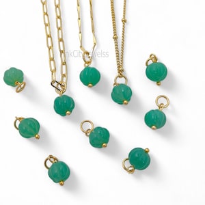 May include: Gold-toned necklaces with green gemstone pendants. The pendants are round with a ribbed texture. Several loose pendants are also scattered around the necklaces. The background is white.