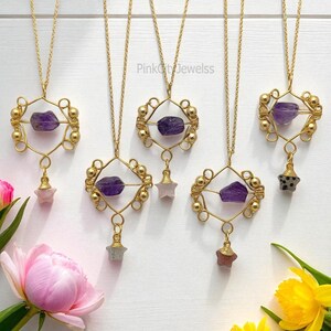 Peut inclure: Colliers dorés avec des pierres d'améthyste et des pendentifs en forme d'étoile. Les colliers ont un design géométrique avec de petites perles dorées. L'image comprend des fleurs roses et jaunes.