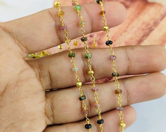 Puede incluir: Una cadena de oro con pequeñas cuentas de piedras preciosas de colores. La cadena está hecha de alambre chapado en oro y presenta una variedad de colores, incluyendo rosa, verde, negro y amarillo.