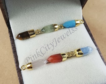 May include: Five gemstone pendants with gold caps, arranged in a line in a white velvet box. The gemstones are tiger's eye, green aventurine, turquoise, rose quartz, and blue lace agate.
