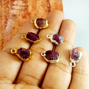 Puede incluir: Seis colgantes de piedra de rubí en bruto con engastes de oro y plata. Las piedras de rubí son de color rojo intenso y tienen una textura rugosa y natural. Los colgantes son perfectos para la elaboración de joyas o la artesanía.