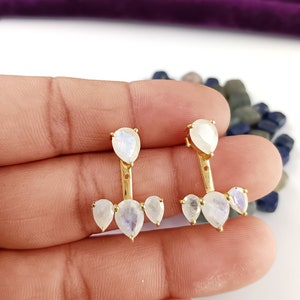 Puede incluir: Un par de pendientes de oro con una piedra de luna en forma de lágrima en la parte superior y tres piedras de luna más pequeñas en la parte inferior.