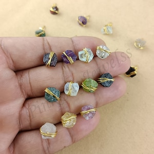 Può includere: Assortimento di 14 ciondoli in pietra grezza avvolti in filo d'oro. Le pietre preziose sono di vari colori, tra cui trasparente, verde, viola, rosso e nero.