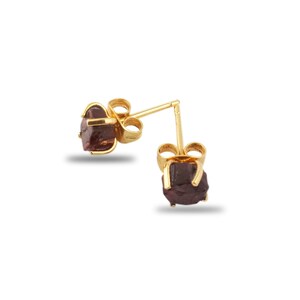May include: A pair of gold stud earrings with a raw, dark red gemstone. The earrings are simple and elegant.