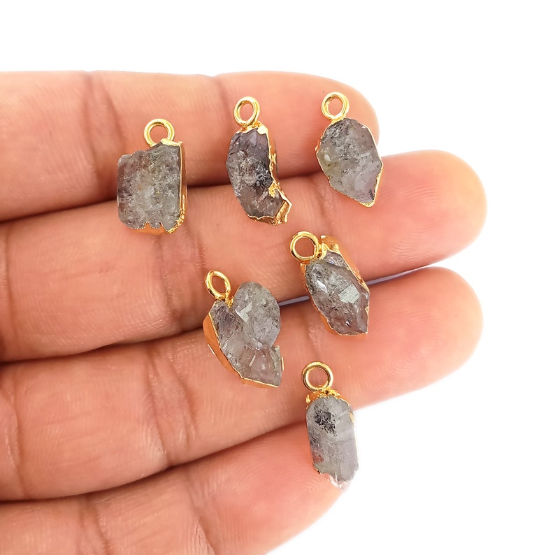 May include: Seven raw crystal pendants with gold-plated bail settings. The crystals are a light gray color and have a rough, natural texture.
