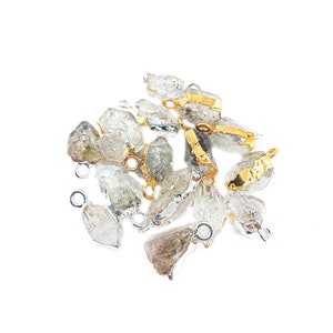 May include: A group of raw crystal pendants with gold and silver accents. The crystals are clear and have a rough, natural texture. The pendants are perfect for jewelry making or crafting.