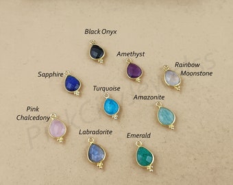 May include: Assortment of gemstone teardrop charms in various colors, including black onyx, amethyst, rainbow moonstone, sapphire, turquoise, amazonite, pink chalcedony, labradorite, and emerald. Each charm features a gold setting and a teardrop-shaped gemstone.