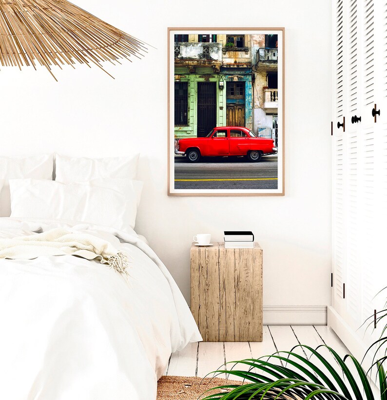 May include: A red vintage car parked in front of a colorful building with peeling paint. The car is in focus, while the building is slightly blurred in the background.