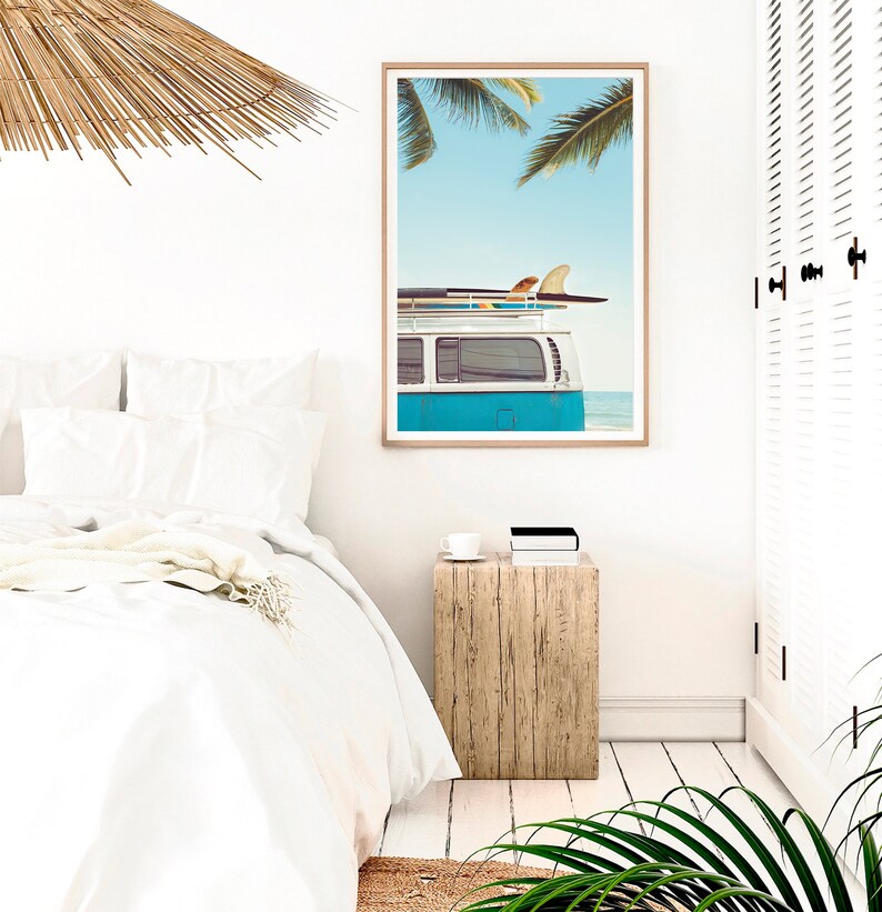 May include: A framed print of a blue vintage van with surfboards on the roof, parked on a beach with palm trees in the background.
