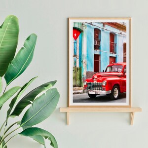May include: A vintage red car parked in front of a blue and green building with a Cuban flag hanging on the wall. The car has a white star on the front grill and a white license plate.