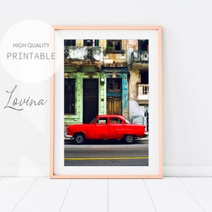 May include: A bright red vintage car parked on a street in front of a colorful building with peeling paint. The building has multiple windows and doors, and the car is in focus.