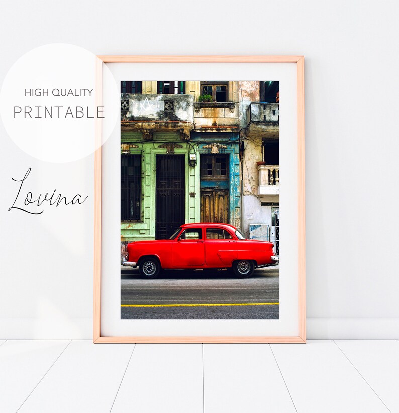 May include: A bright red vintage car parked on a street in front of a colorful building with peeling paint. The building has multiple windows and doors, and the car is in focus.